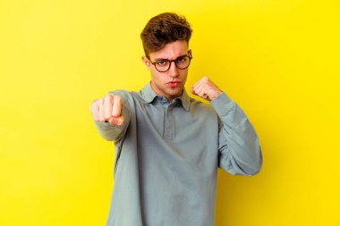 Sarı arka planda izole edilmiş genç beyaz bir adam bir tartışma yüzünden yumruk atıyor, öfkeleniyor, kavga ediyor, boks yapıyor.