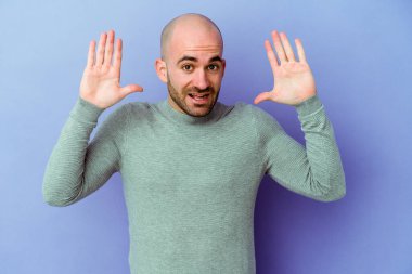 Mor arka planda izole genç beyaz adam hoş bir sürpriz alıyor, heyecanlı ve el kaldırıyor..