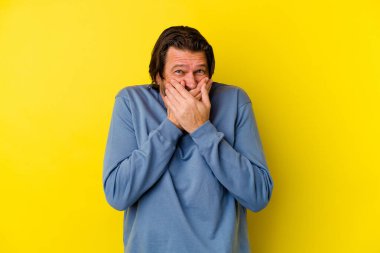 Orta yaşlı beyaz bir adam sarı arka planda izole edilmiş ağzı kapalı ve elleri endişeli görünüyor..