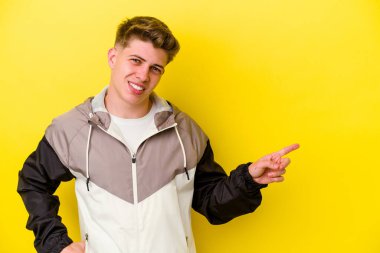 Sarı arka planda izole edilmiş genç beyaz adam işaret parmağıyla işaret ederek gülümsüyor..