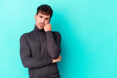 Mavi arka planda izole edilmiş, üzgün ve dalgın hisseden, kopyalama alanına bakan genç beyaz bir adam..