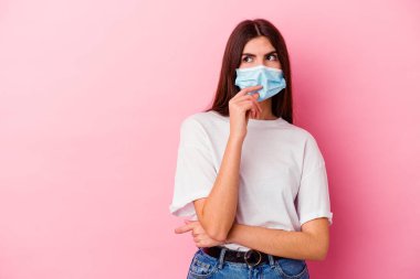 Pembe arka planda izole edilmiş virüs maskesi takan beyaz bir kadın bir şeyin fotokopi odasına baktığını düşünüyor..