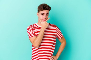 Kafkasyalı genç bir adam mavi arka planda izole edilmiş. Bir strateji planlıyor, bir iş yolu düşünüyor..