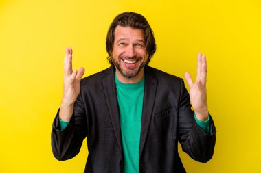Sarı arka planda izole edilmiş orta yaşlı beyaz bir adam hoş bir sürpriz alıyor, heyecanlı ve el kaldırıyor..