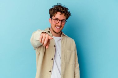 Gözlük takan genç beyaz adam mavi arka planda izole edilmiş önü işaret eden neşeli gülümsemeler..