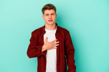 Kafkasyalı genç adam mavi arka planda izole edilmiş yemin ediyor, elini göğsüne koyuyor..