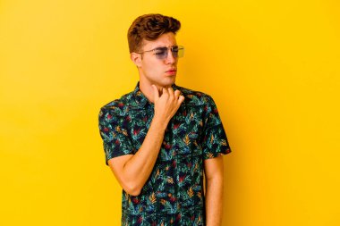 Sarı arka planda izole edilmiş Hawaii gömleği giyen beyaz bir adam virüs veya enfeksiyon yüzünden boğazında ağrı hissediyor..