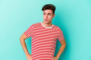 Mavi arka planda soyutlanmış genç beyaz bir adam gülümsüyor, neşeli ve keyifli görünüyor..