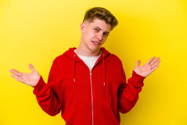 Kafkasyalı genç adam sarı arka planda izole edilmiş. Kafası karışmış ve omuz silkiyor. Kopya alanını tutmak için..