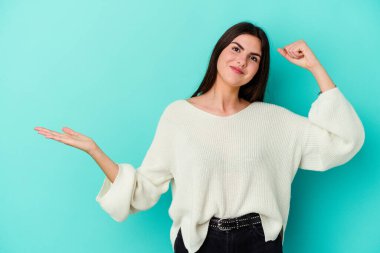 Mavi arka planda izole edilmiş beyaz bir kadın avuç içinde fotokopi alanı tutuyor, el üstünde tutuyor. Şaşırmış ve mutlu..