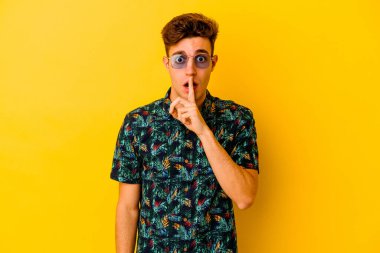Sarı arka planda izole edilmiş Hawaii gömleği giyen genç beyaz bir adam bir sır saklıyor ya da sessizlik istiyor..