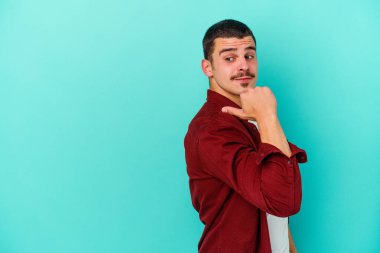 Kafkasyalı genç adam mavi arka plan noktalarında izole edilmiş başparmak uzakta, gülüyor ve kaygısız.