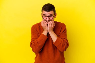 Sarı arka planda izole edilmiş, tırnak yiyen, gergin ve endişeli genç beyaz bir adam..