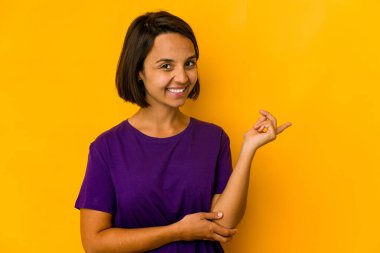Sarı renkte izole edilmiş genç İspanyol kadın işaret parmağıyla işaret ederek gülümsüyor..