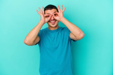 Mavi arka planda izole edilmiş genç beyaz adam gözlerinde sorun olmadığını gösteriyor.