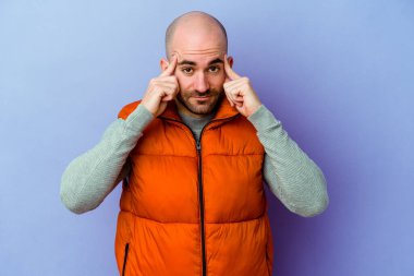 Mor arka planda izole genç, beyaz kel adam bir göreve odaklanmış, parmaklarını işaret ediyor..