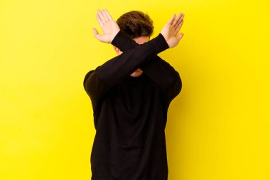 Sarı arka planda izole genç beyaz adam iki kolu çapraz tutuyor, inkar kavramı.