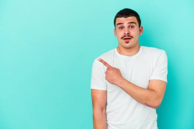 Mavi arka planda izole edilmiş genç beyaz adam yan tarafı işaret ediyor.