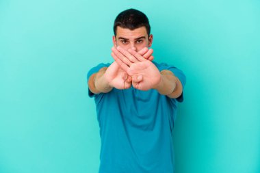Kafkasyalı genç adam mavi arka planda izole edilmiş bir şekilde inkar hareketi yapıyor.