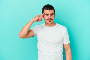 Mavi arka planda izole edilmiş genç beyaz bir adam şakağı parmağıyla işaret ediyor, düşünüyor ve bir göreve odaklanıyor..