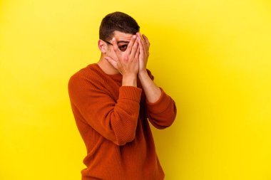 Sarı arka planda izole edilmiş genç beyaz adam parmaklarıyla gözünü kırp korkmuş ve gergin..