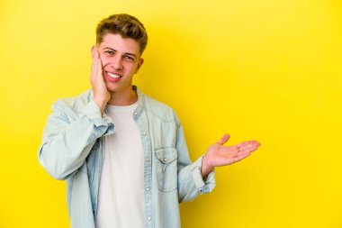 Sarı arka planda izole edilmiş genç beyaz bir adam bir avuç içinde fotokopi alanı tutuyor, el üstünde tutuyor. Şaşırmış ve mutlu..