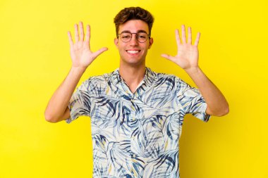 Sarı arka planda izole edilmiş genç beyaz adam on numarayı elleriyle gösteriyor..
