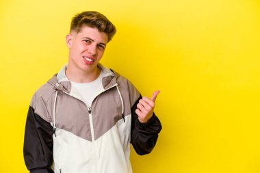 Sarı arka planda izole edilmiş genç beyaz adam işaret parmağıyla fotokopi alanını işaret ederek şok oldu..