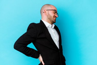 Genç, beyaz, kel bir adam mavi arka planda izole edilmiş ve sırt ağrısı çekiyor..