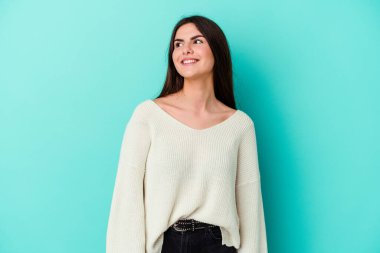 Genç beyaz kadın mavi arka planda izole edilmiş rahat ve mutlu bir şekilde gülüyor, boynunda dişlerini gösteriyor..
