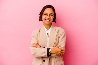 Pembe arka planda soyutlanmış, kendine güveni tam, kararlılıkla kollarını kavuşturan genç iş kadını..