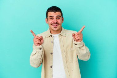 Mavi arka planda izole edilmiş genç beyaz adam farklı kopya alanlarını gösteriyor, birini seçiyor, parmaklarıyla gösteriyor.