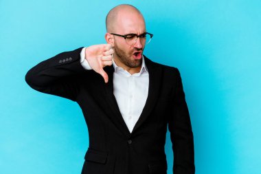 Genç, beyaz, kel bir adam mavi arka planda izole edilmiş. Baş parmağını aşağı gösteriyor ve hoşlanmadığını ifade ediyor..