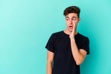 Mavi arka planda izole edilmiş genç beyaz bir adam gizli bir sıcak fren haberi veriyor ve yana bakıyor.