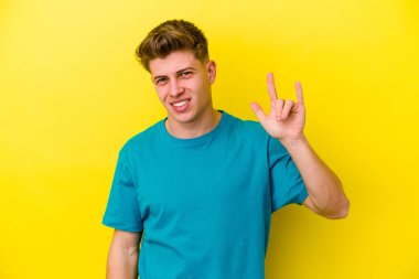 Sarı arka planda izole edilmiş genç beyaz adam boynuzlarını devrim konsepti olarak gösteriyor..