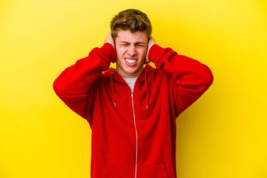 Kafkasyalı genç adam sarı arka planda izole edilmiş kulakları kulaklarıyla kapatıyor çok fazla ses duymamaya çalışıyor..