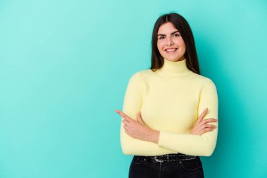 Mavi arka planda izole edilmiş genç beyaz kadın işaret parmağıyla işaret ederek gülümsüyor..
