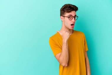 Kafkasyalı genç adam mavi arka plan noktalarında izole edilmiş başparmak uzakta, gülüyor ve kaygısız.