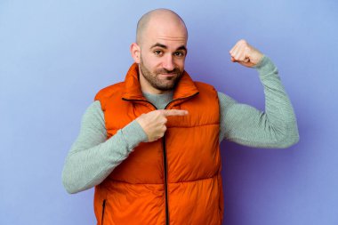 Mor arka planda yalıtılmış genç, beyaz, kel bir adam kollarıyla güçlü bir hareket gösteriyor, kadınsı gücün sembolü.