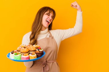 Genç pasta şefi kadın sarı arka planda izole edilmiş zafer kazandıktan sonra yumruğunu kaldırıyor, kazanan konsept.
