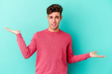 Kafkasyalı genç adam mavi arka planda izole edilmiş. Kafası karışmış ve omuz silkiyor. Kopya alanını tutmak için..