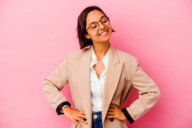 Genç iş kadını, pembe arka planda izole edilmiş, kendine güveni tam, ellerini kalçasında tutuyor..