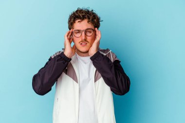 Mavi arka planda izole edilmiş gözlük takan genç beyaz adam şakaklara dokunuyor ve baş ağrısı çekiyor..