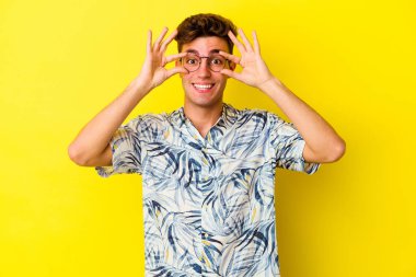 Sarı arka planda izole edilmiş genç beyaz adam bir başarı fırsatı bulmak için gözlerini açık tutuyor..