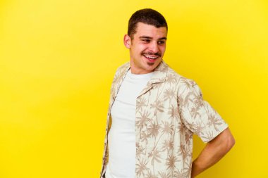 Sarı arka planda izole edilmiş genç beyaz adam mutlu bir şekilde gülüyor ve ellerini karnının üstünde tutarak eğleniyor..