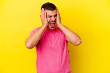 Kafkas asıllı genç adam sarı arka planda izole edilmiş kulakları kulaklarıyla kapatıyor çok fazla ses duymamaya çalışıyor..