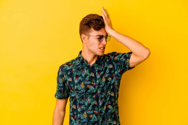 Sarı arka planda izole edilmiş Hawaii gömleği giyen genç beyaz bir adam bir şeyi unutuyor, alnına avuç içi ile vuruyor ve gözlerini kapıyor..