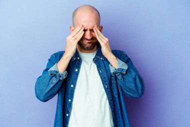 Kafkasyalı kel bir adam mor arka planda izole edilmiş, başı ağrıyor, yüzüne dokunuyor..