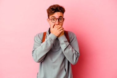 Pembe arka planda izole edilmiş genç bir öğrenci elleriyle ağzını kapatırken şok oldu..