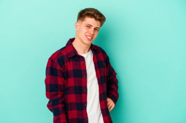 Kafkasyalı genç, mavi arka planda izole edilmiş. Kendine güvenen, kalçaları tutan biri..